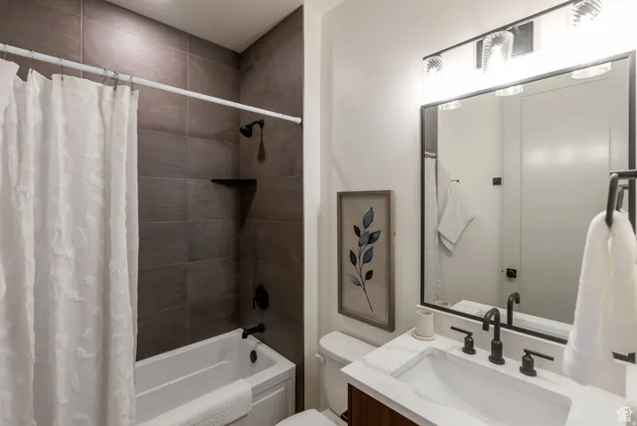 Bathroom featuring a bathtub with dark-toned tile surround, matte black shower fixtures, a single vanity with a white countertop, and a large mirror with integrated lighting