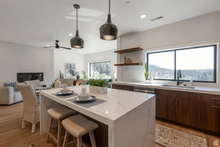 Kitchen featuring a waterfall island, dark wood-finish cabinetry, built-in stainless steel appliances, and suspended pendant lighting