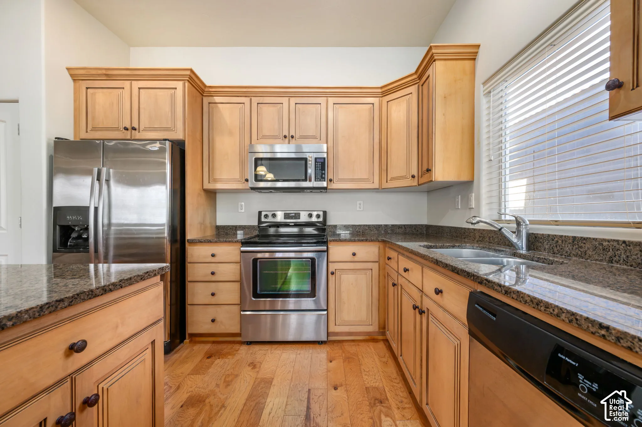 Wood-finish flooring with light wood cabinetry, stainless steel appliances, and dark stone countertops