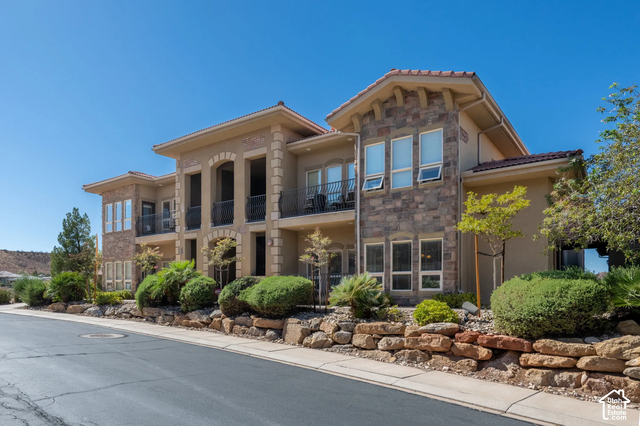 Multi-level residential structure featuring a stucco exterior, stone facade accents, and a tile roof