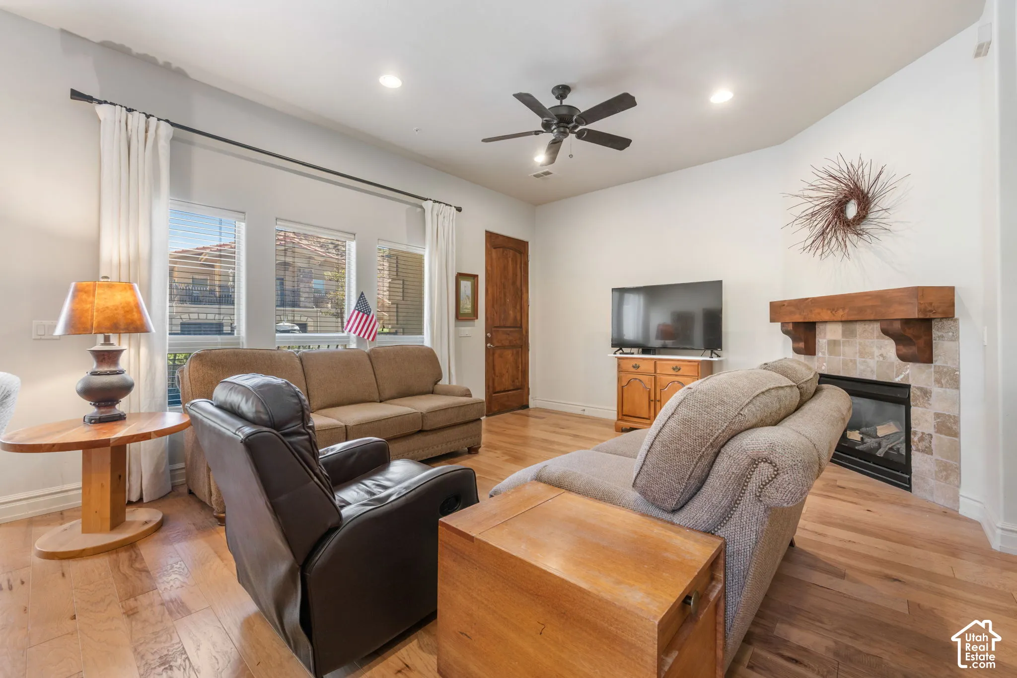 Corner fireplace with tiled surround and wood mantel, recessed lighting, ceiling fan, wood-finish flooring, and multiple windows