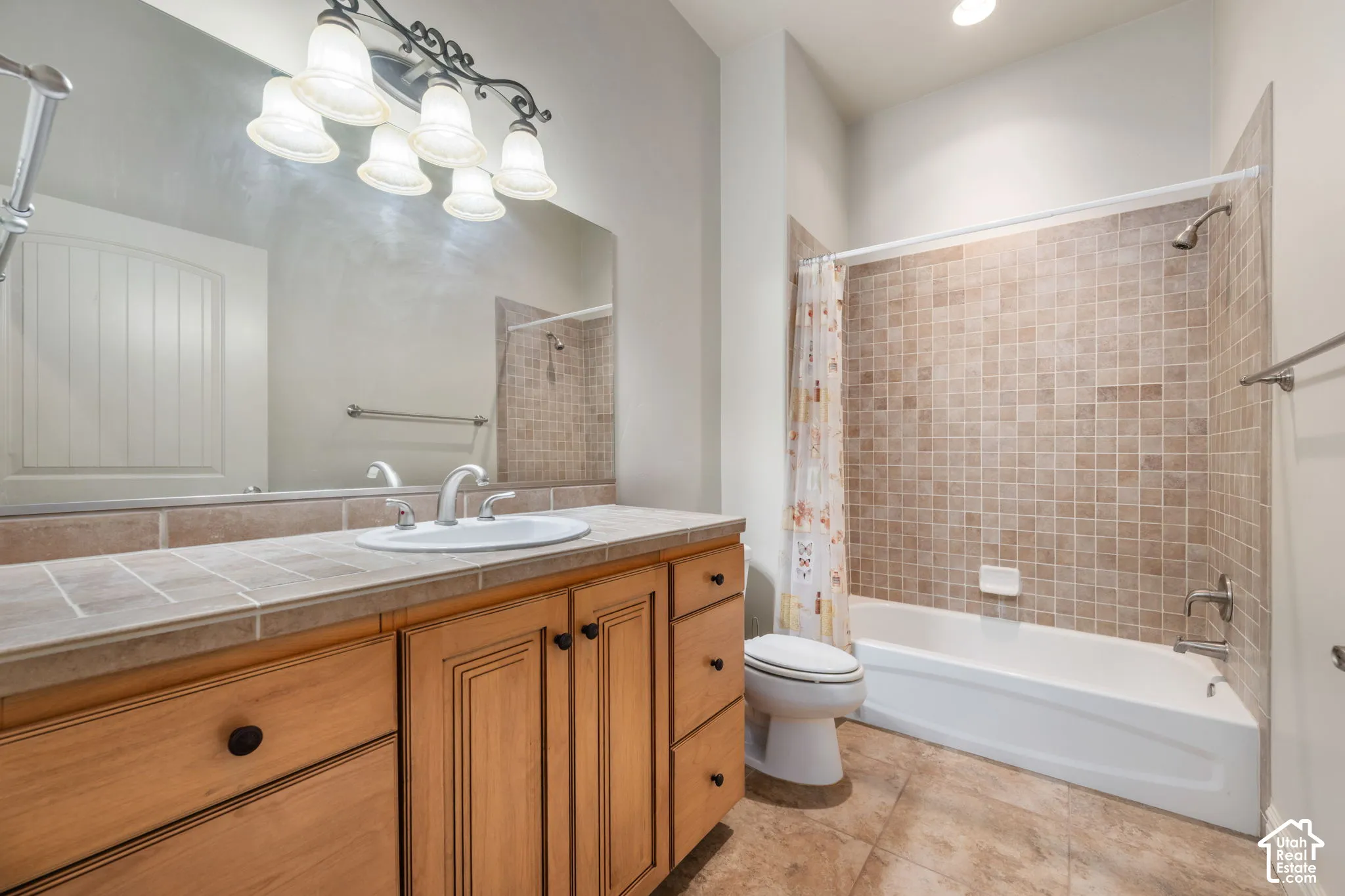 Wood-finish vanity with an integrated sink, tile countertop, and large vanity mirror