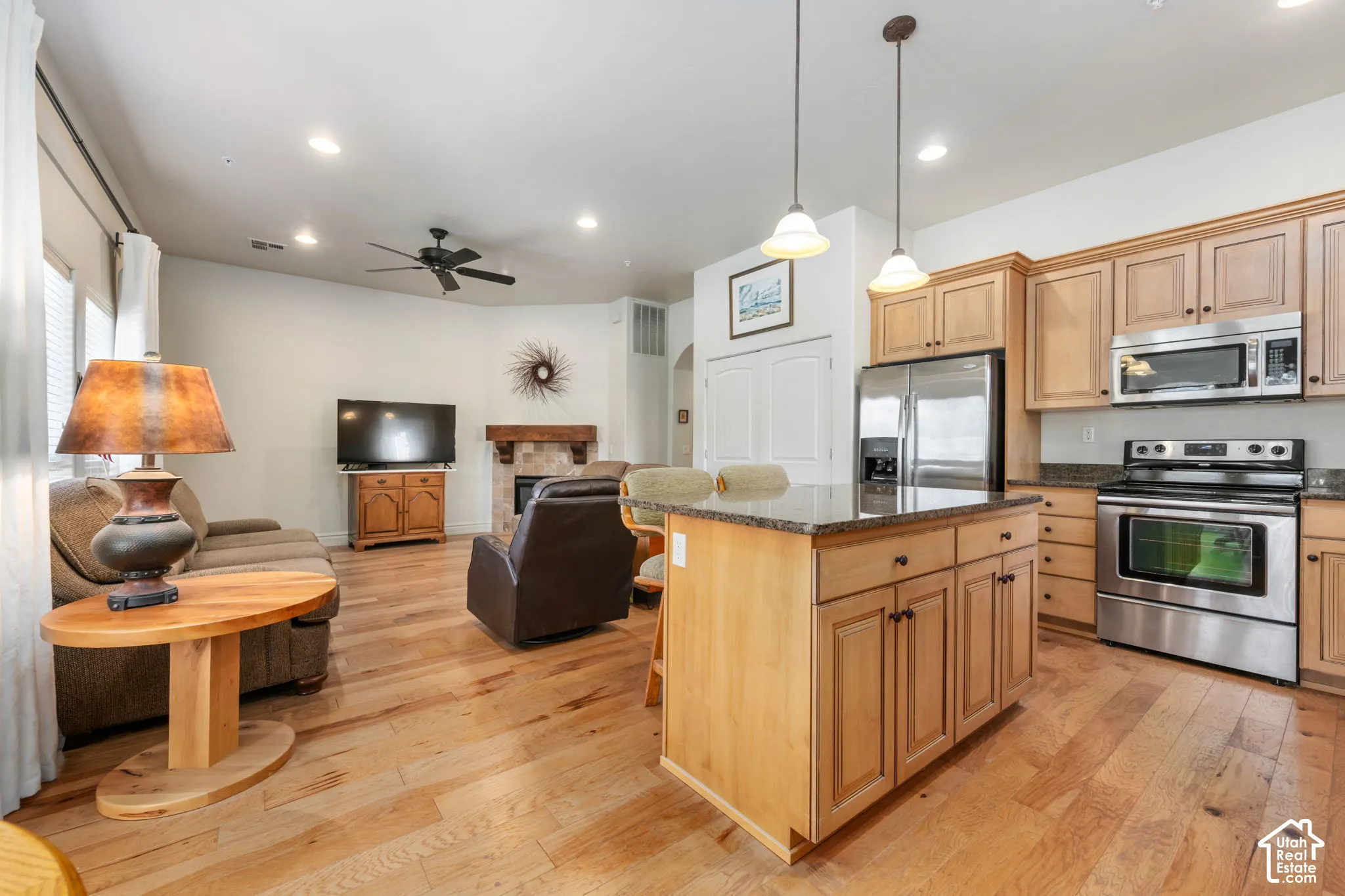 Open-concept living space with wood-finish flooring, a kitchen island with stone-finish countertop, and stainless-steel appliances