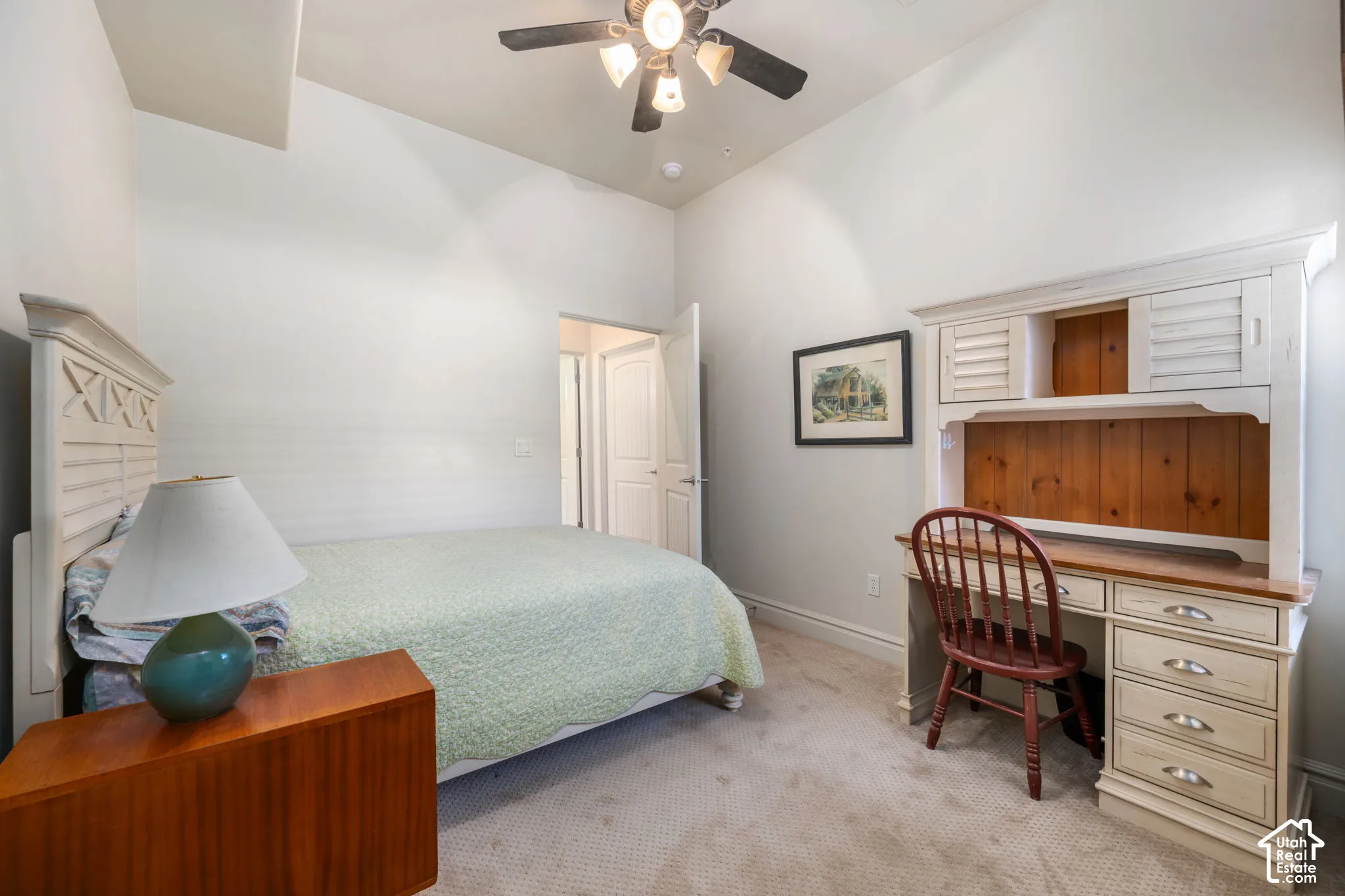 Vaulted ceiling, ceiling fan with integrated lighting, built-in desk with shelving, and light-colored carpeting