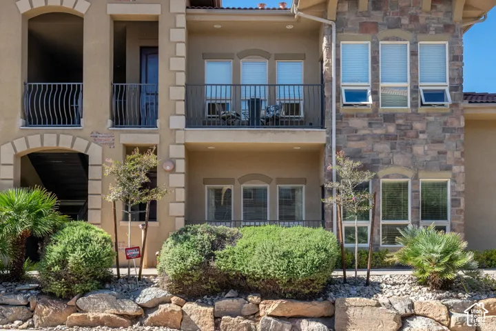 Stucco exterior with stone accents, wrought iron balconies, arched doorways, and mature landscaping