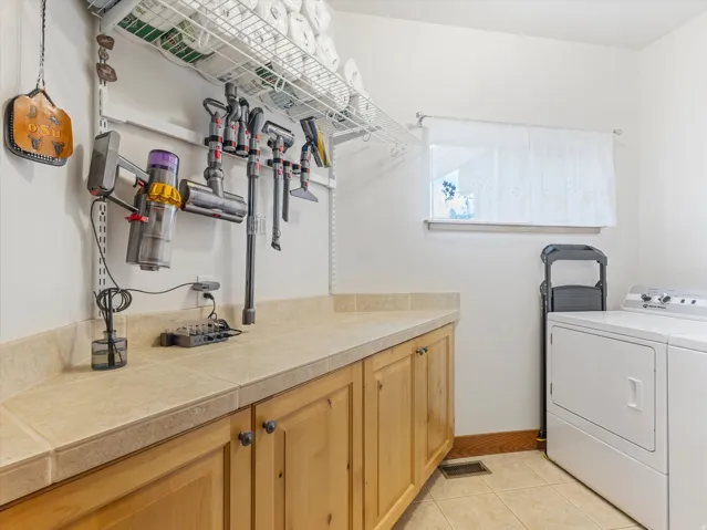 Functional utility area featuring light wood-finish cabinetry with dark hardware, a light-toned countertop, and a window with natural light