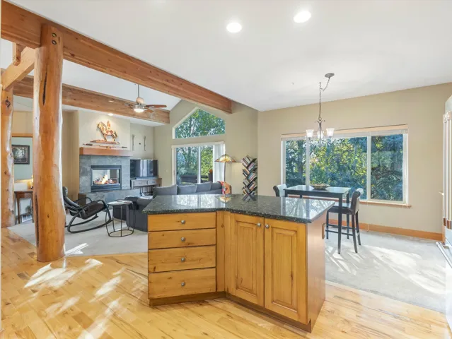 Kitchen island with granite countertop, wood-finish flooring, vaulted ceiling with wood beams, and a stone-faced fireplace