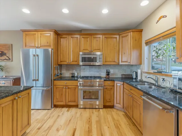 Hardwood flooring, wood cabinetry, stainless steel appliances, dark countertops, and recessed lighting