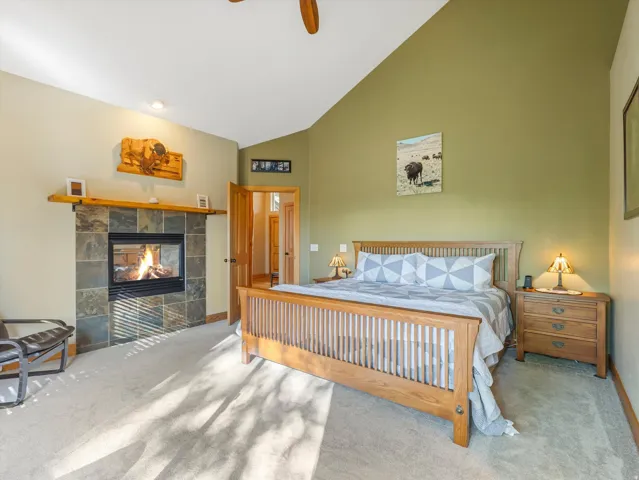 Vaulted ceiling, carpeted flooring, built-in fireplace with stone surround, and wood-finish door frames