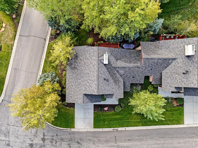Asphalt shingle roofing, multiple mature trees, manicured lawns, and concrete sidewalks