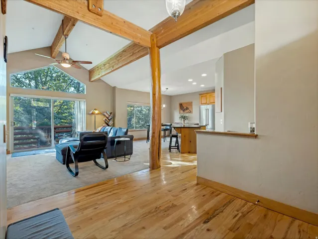 Open-concept living area with vaulted ceilings, exposed wood beams, wood-finish flooring, and a sliding glass door leading to an outdoor space