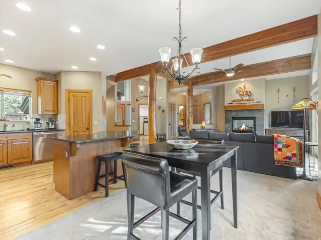 Kitchen island with stone countertop, stainless steel appliances, wood-finish flooring, exposed wood beams, and a stone-clad fireplace