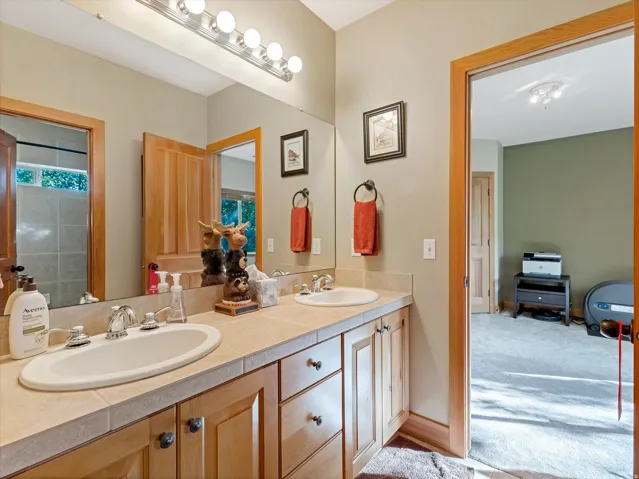 Dual vanity with undermount sinks, tile countertop, wood-finish cabinetry, and full-width mirror
