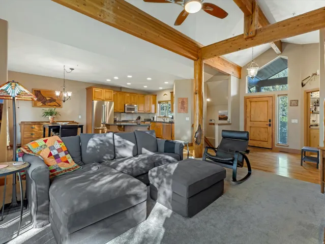 Vaulted ceiling with exposed wood beams, wood-finish flooring, stainless steel appliances, kitchen island with seating, and wood cabinetry