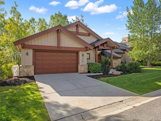 Two-car garage with panel door, stone base exterior, covered front entry, and mature landscaping