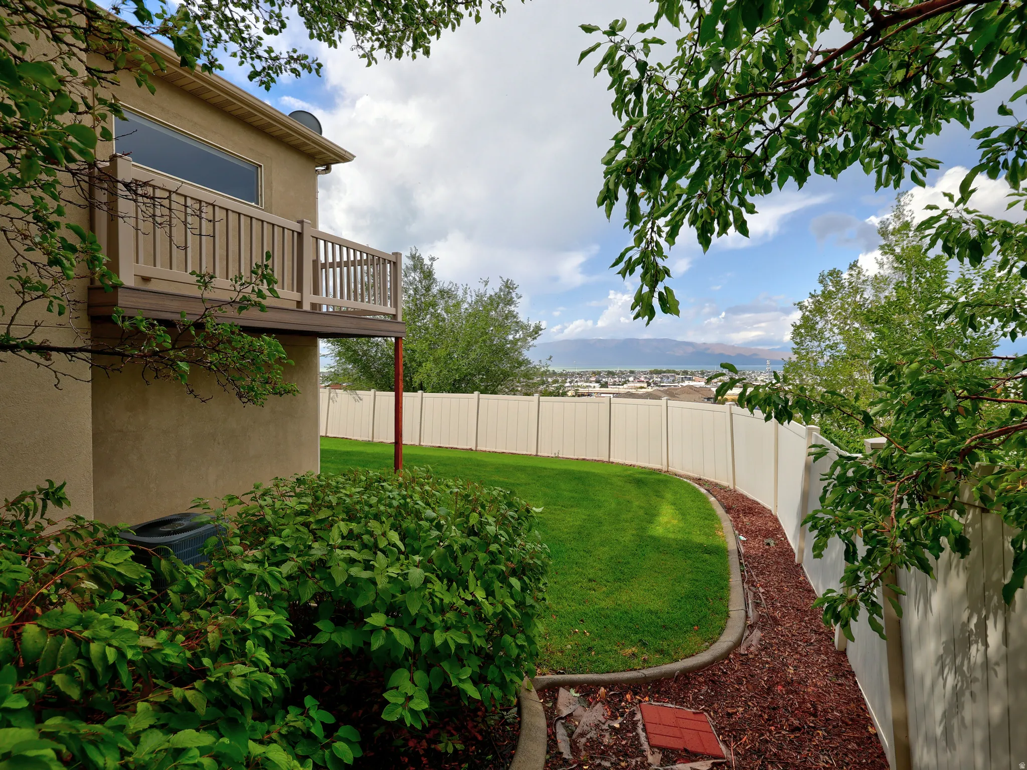 Second-story balcony with composite decking and railing, stucco exterior, expansive lawn, and white privacy fencing