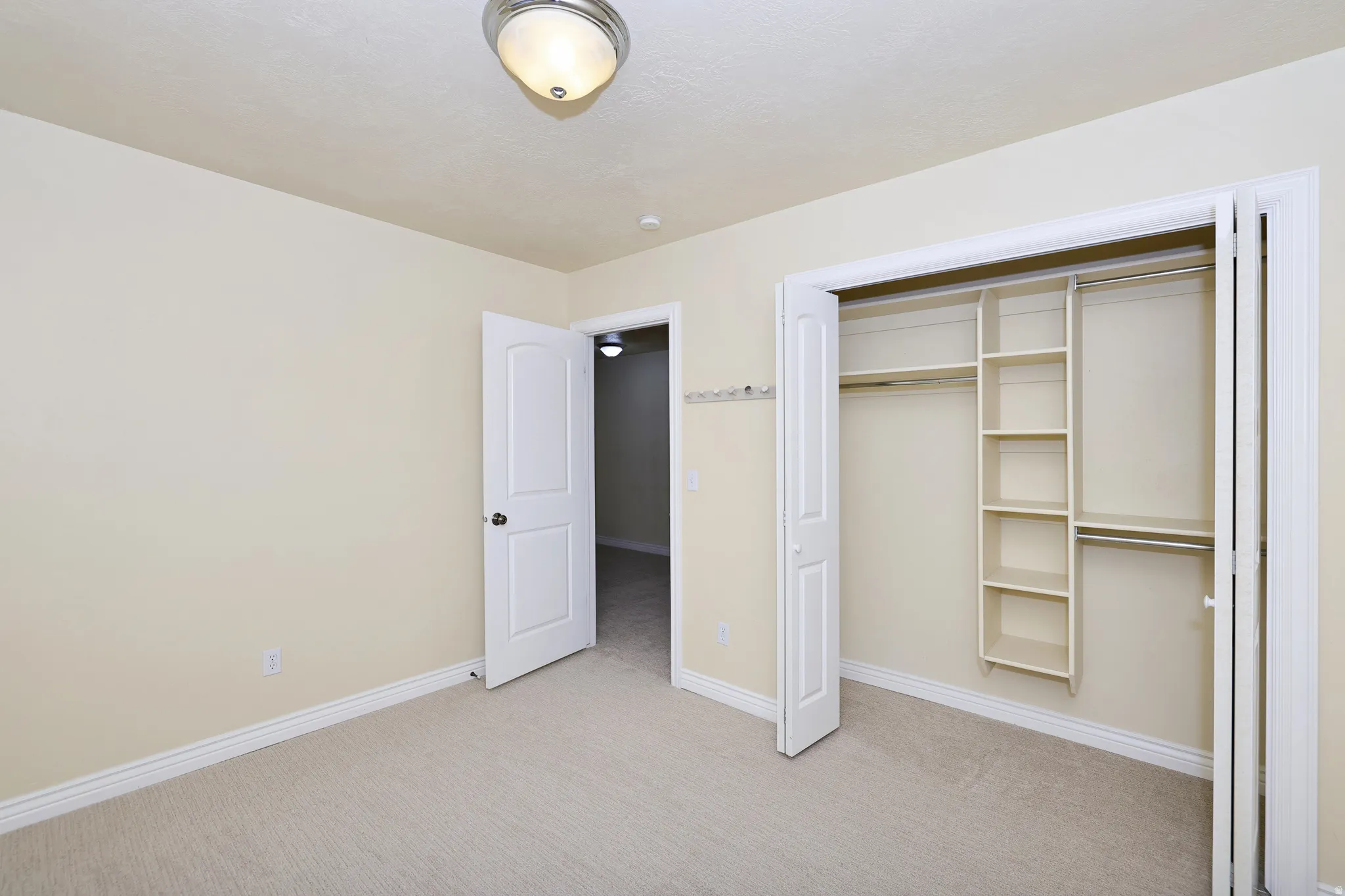 Carpeted flooring, bi-fold closet doors, built-in closet shelving, interior door with black hardware, and a semi-flush mount ceiling fixture