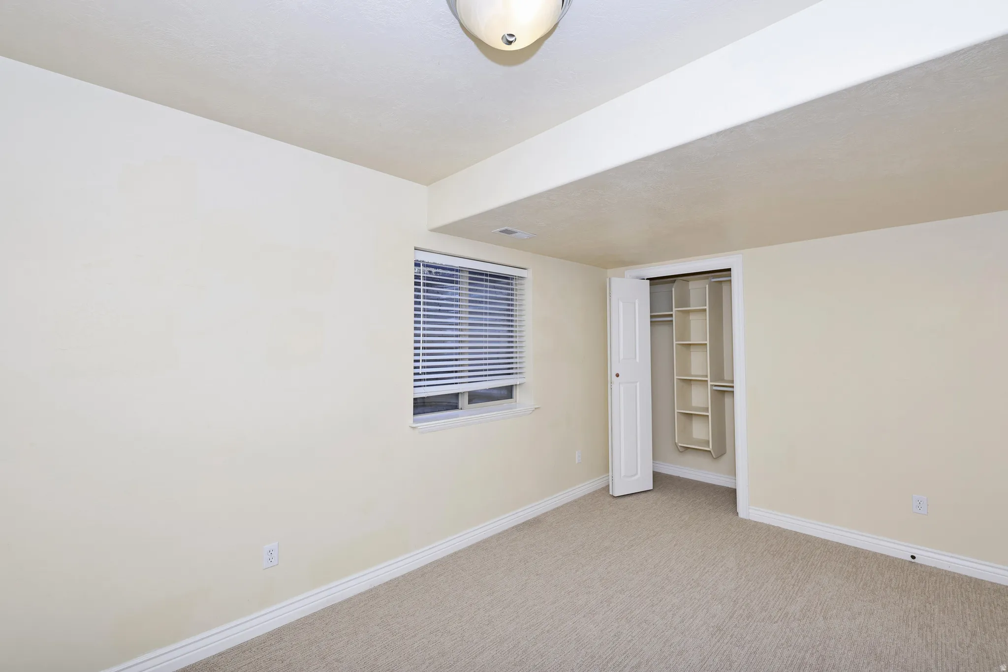 Neutral-toned walls, carpeted flooring, and a built-in closet with shelving