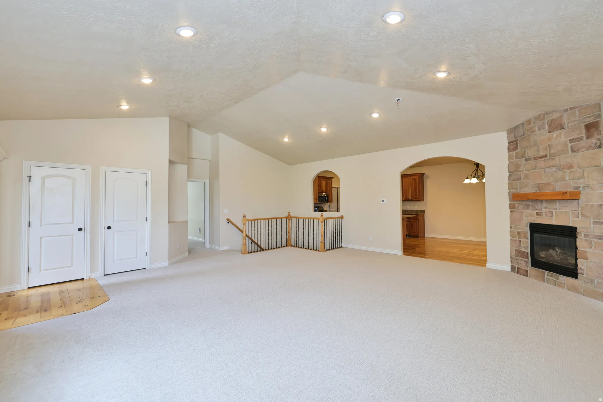 Vaulted ceiling with recessed lighting, stone-clad fireplace with mantel, arched doorways, and wood-finish flooring