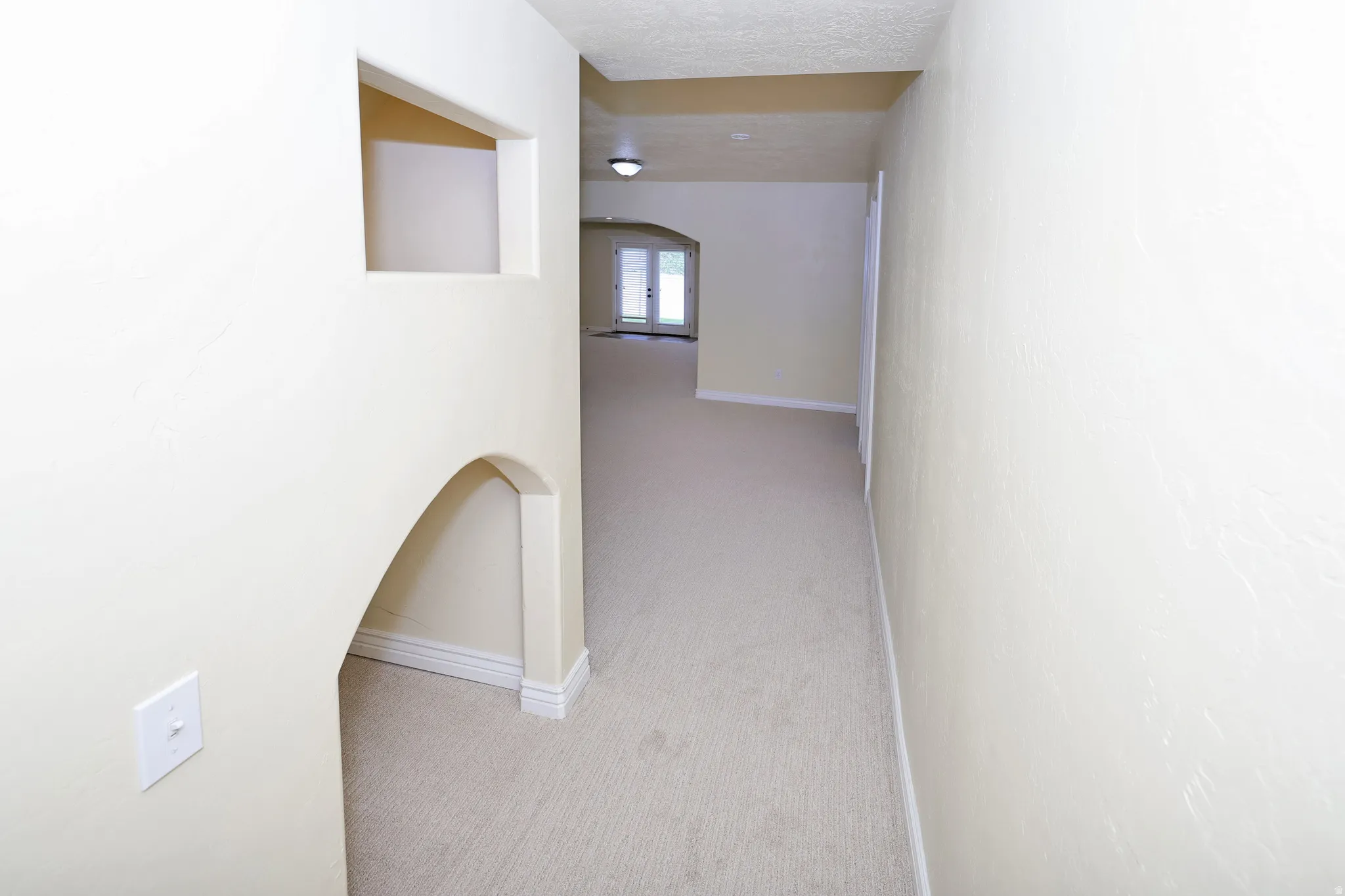 Carpeted hallway with arched architectural detail and recessed ceiling lighting