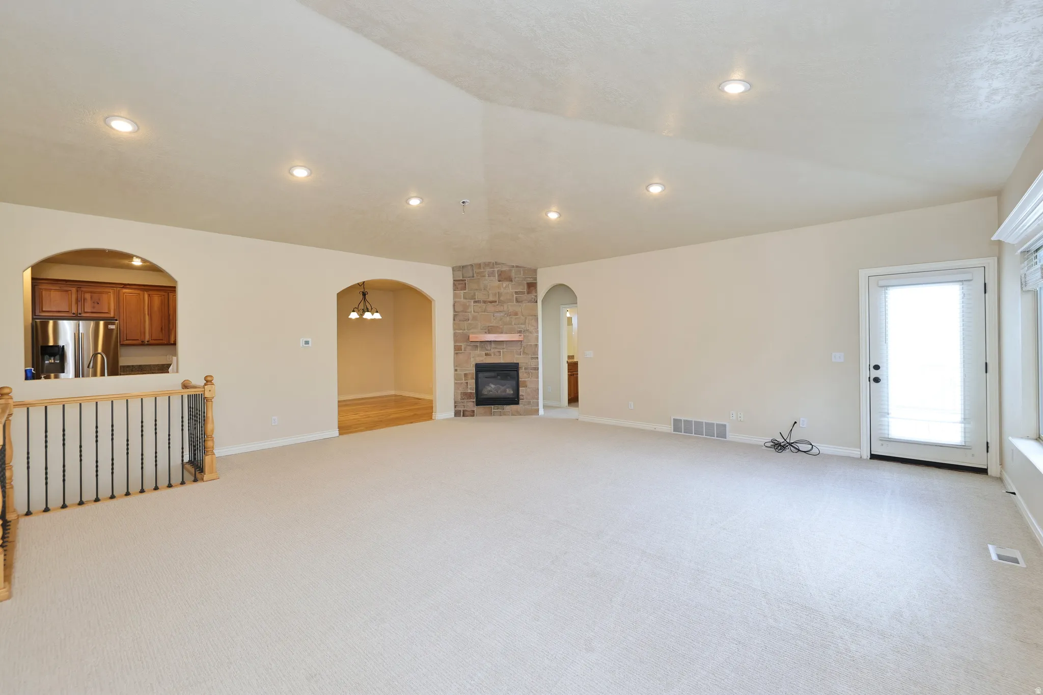 Vaulted ceiling with recessed lighting, stone-clad fireplace with mantel, arched doorways, and a white paneled door with integrated blinds