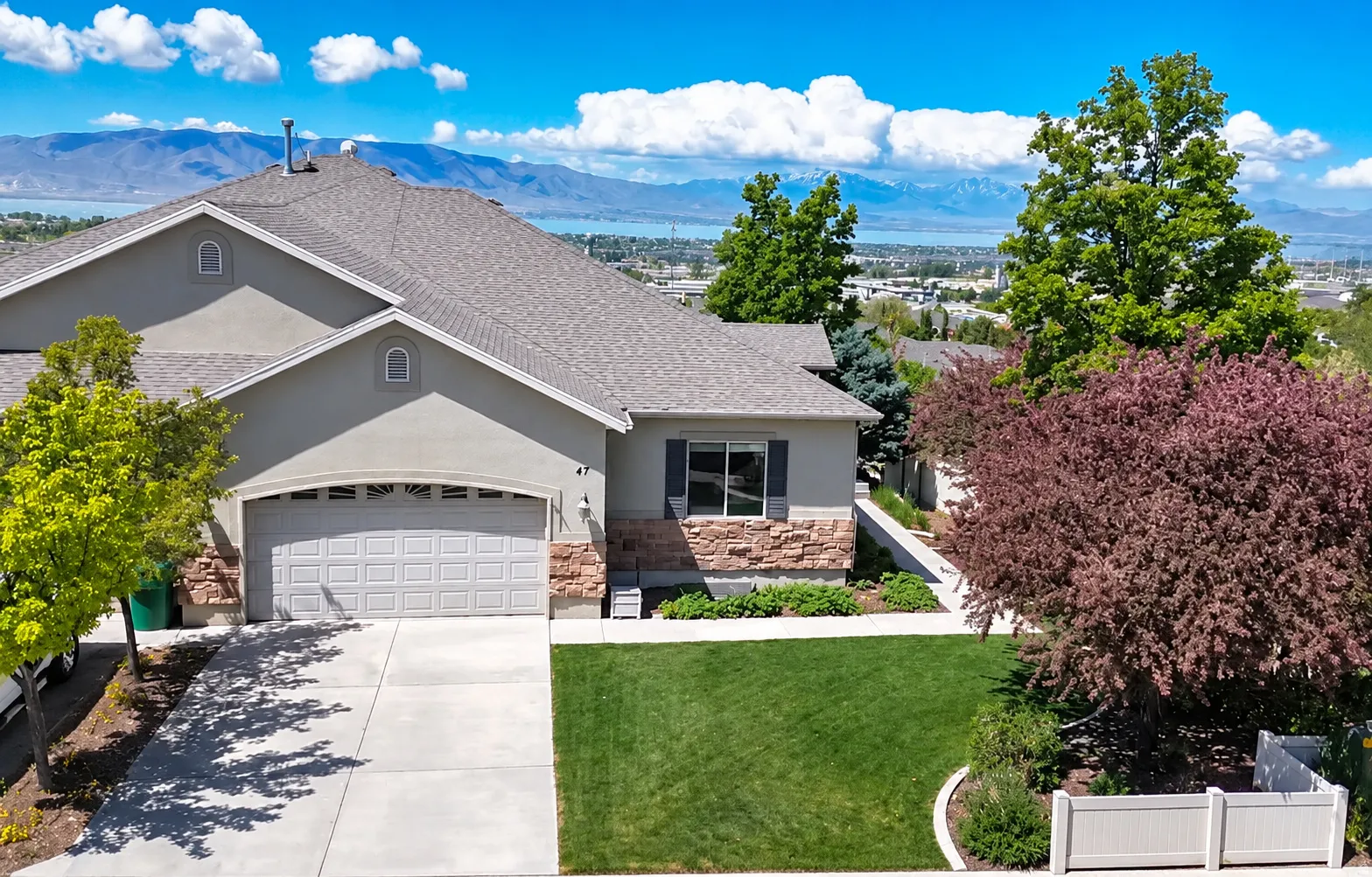 Stucco exterior with stone accents, attached garage, concrete driveway, front lawn, and mature landscaping