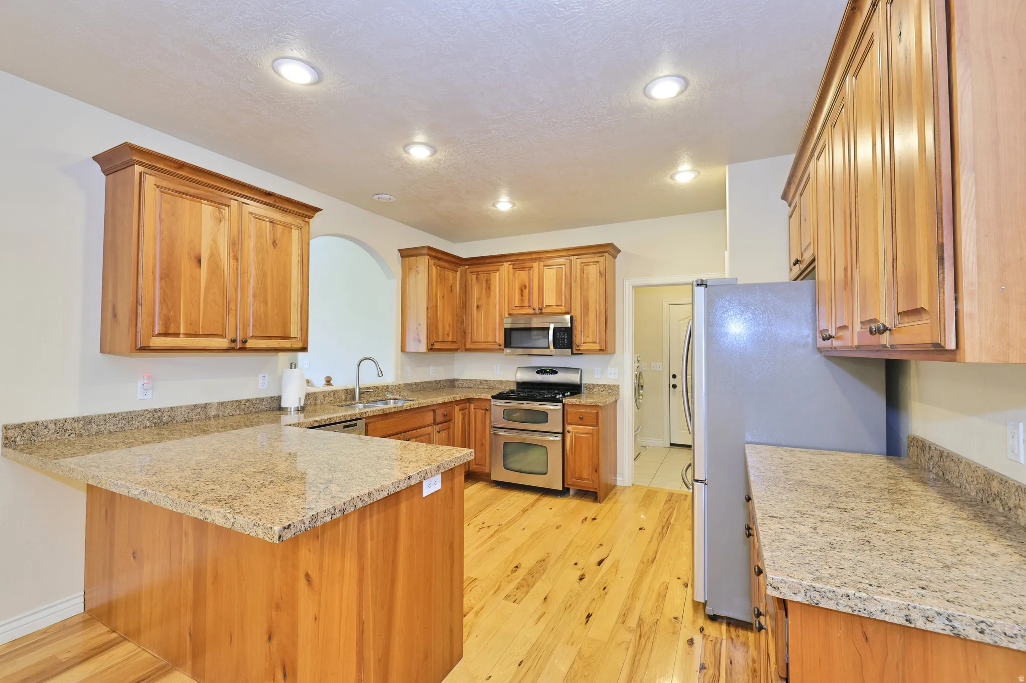 Wood-finish cabinetry, stainless steel appliances, granite countertops, wood-finish flooring, and recessed lighting