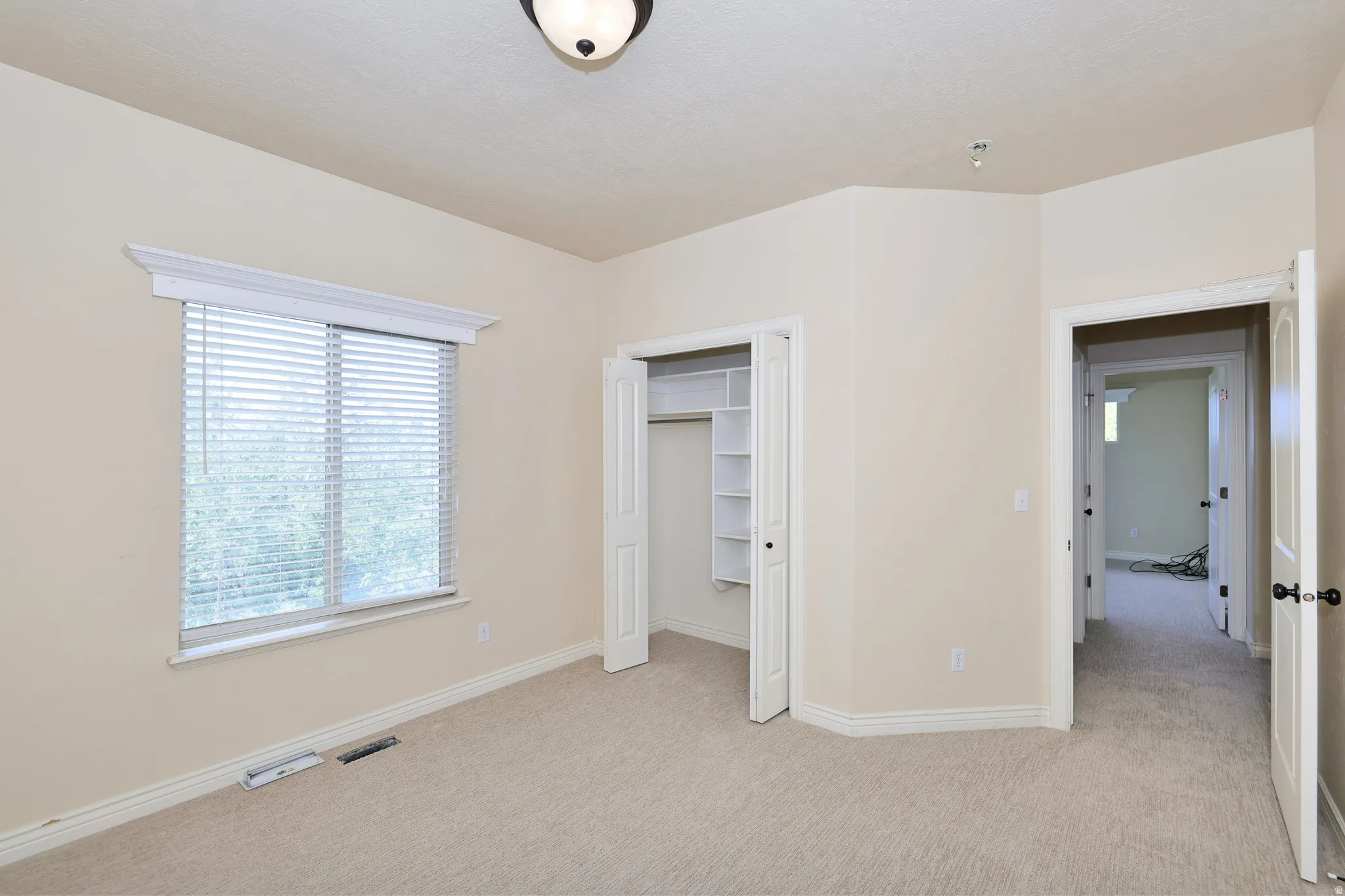 Plush carpeted flooring, window with blinds, built-in closet shelving, ceiling-mounted light fixture, and solid interior doors