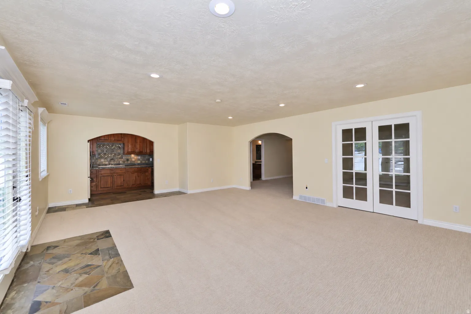 Recessed lighting, arched doorways, French doors, wood-finish cabinetry, and stone flooring accents