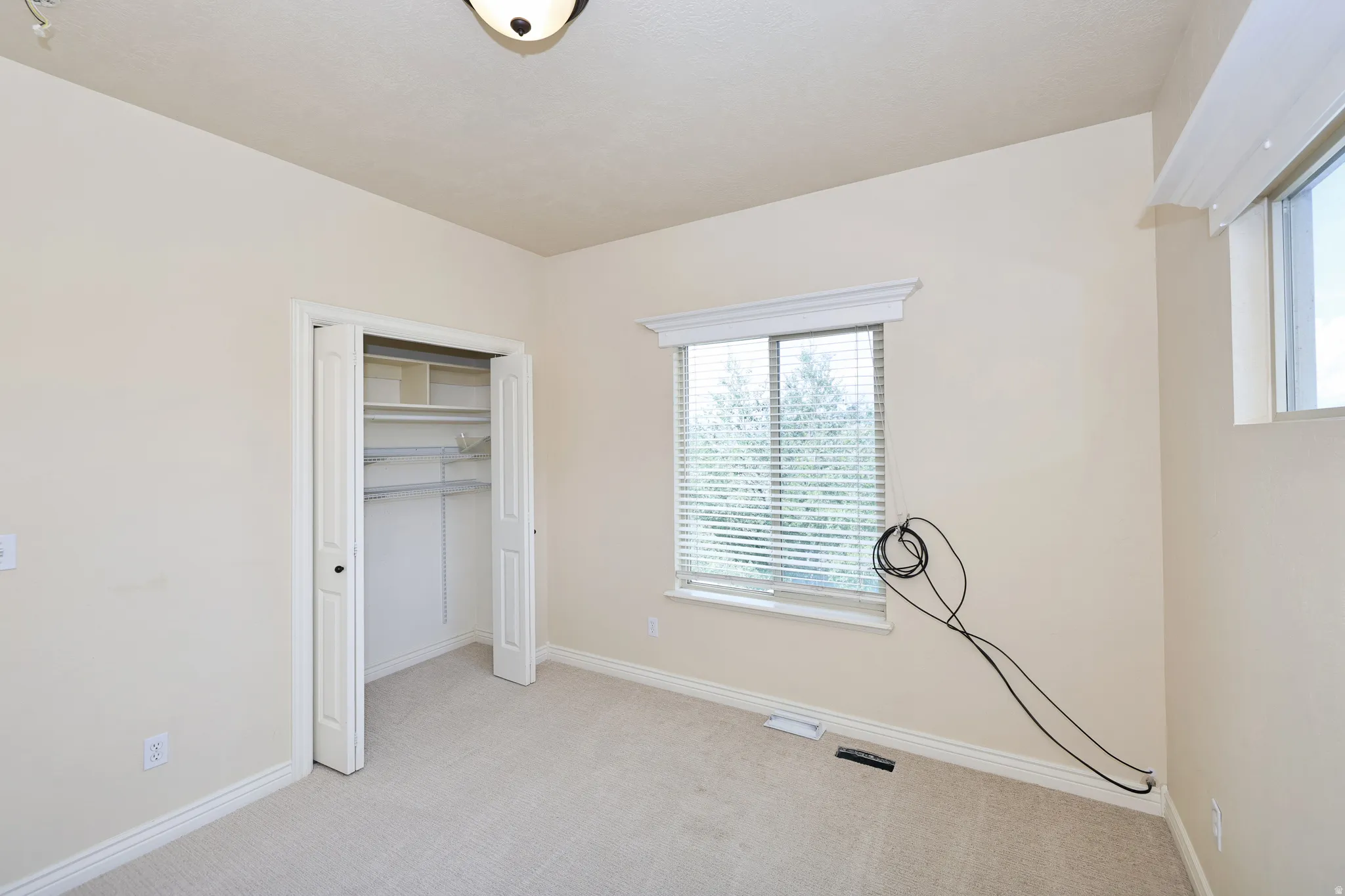Carpeted room with a bi-fold closet, multiple windows, and a flush mount ceiling light