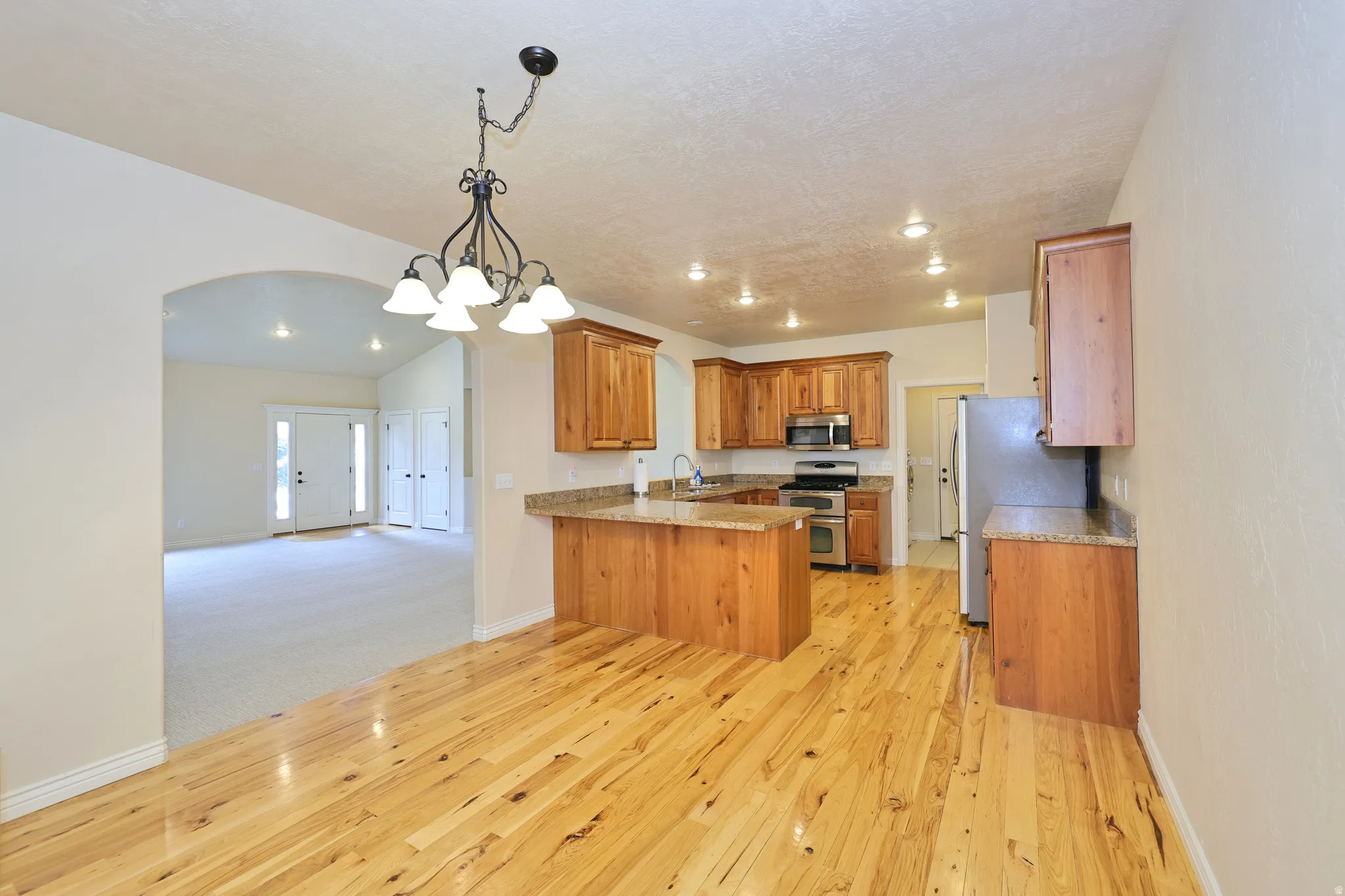 Hardwood flooring, wood cabinetry, stainless steel appliances, recessed lighting, and a kitchen island with seating