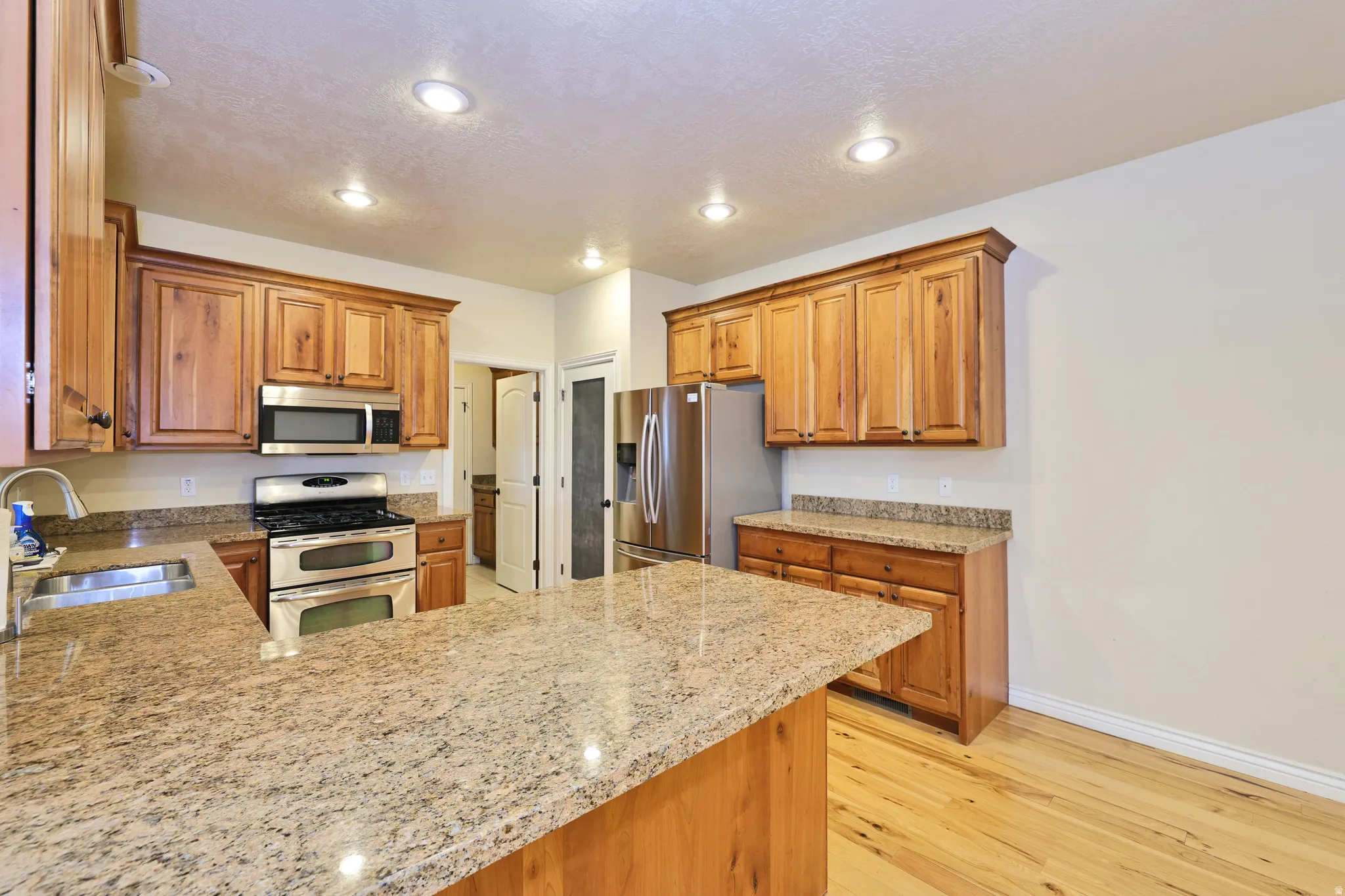 Kitchen featuring wood cabinetry, light-toned countertops, stainless steel appliances, and recessed lighting
