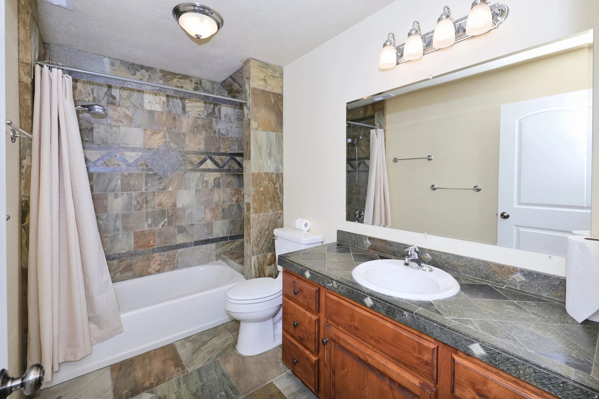 Bathroom featuring a built-in tub with tile surround, wood-finish vanity with an integrated sink, broad mirror, and overhead vanity lighting