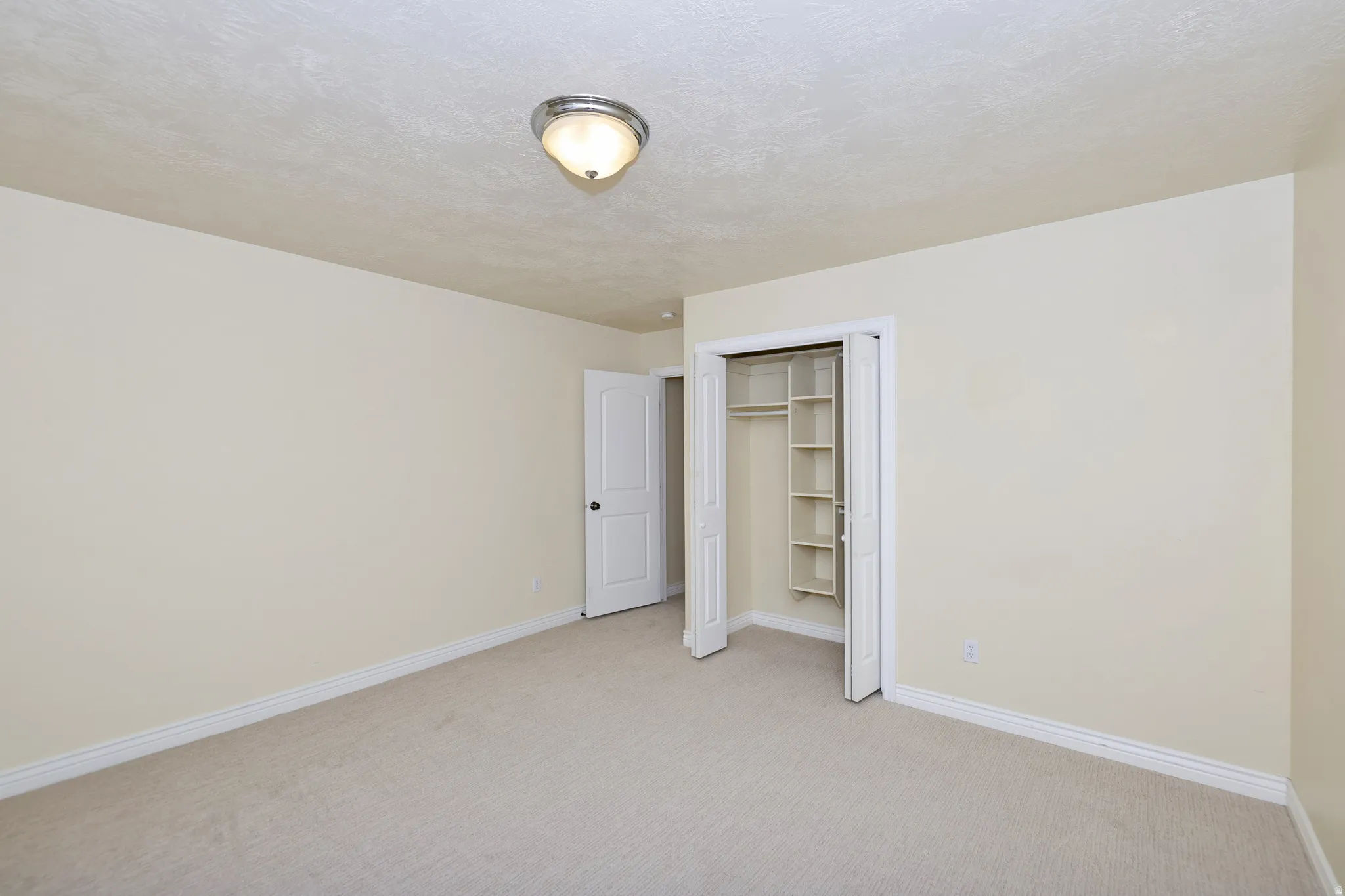 Neutral-toned carpet flooring, light-colored wall paint, white trim, and a built-in closet with shelving