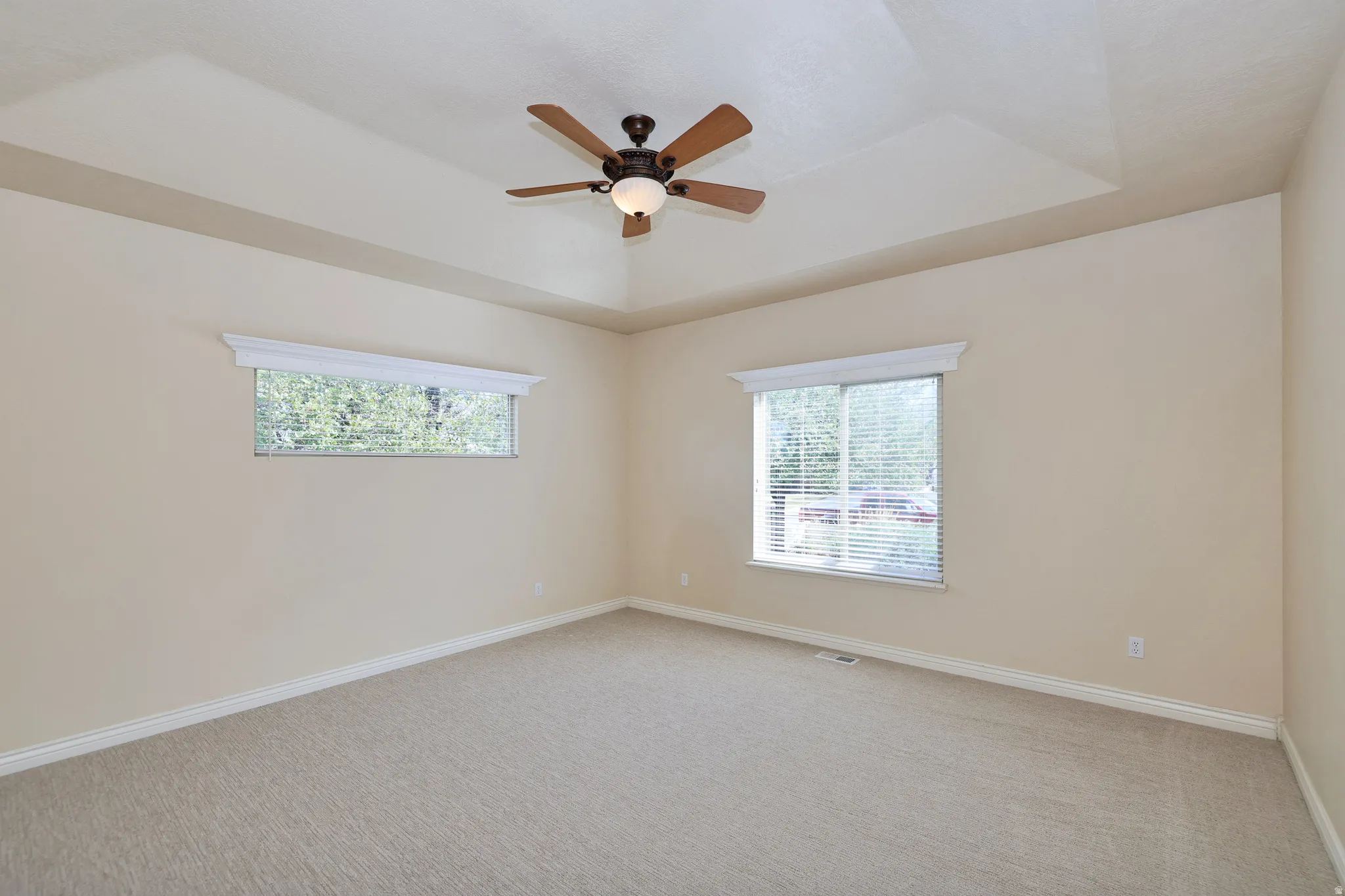 Tray ceiling featuring a ceiling fan with integrated lighting, two windows with blinds, and neutral carpet flooring