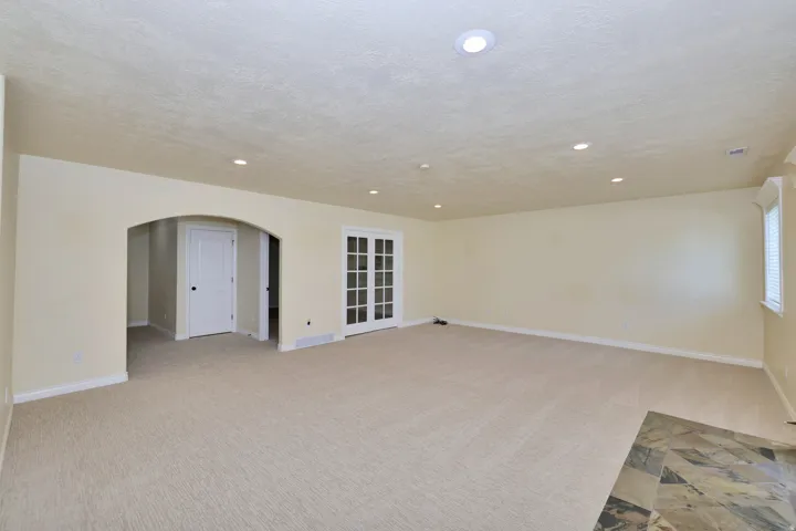 Recessed lighting illuminates the carpeted room, featuring an arched doorway, French doors, and a tiled floor section