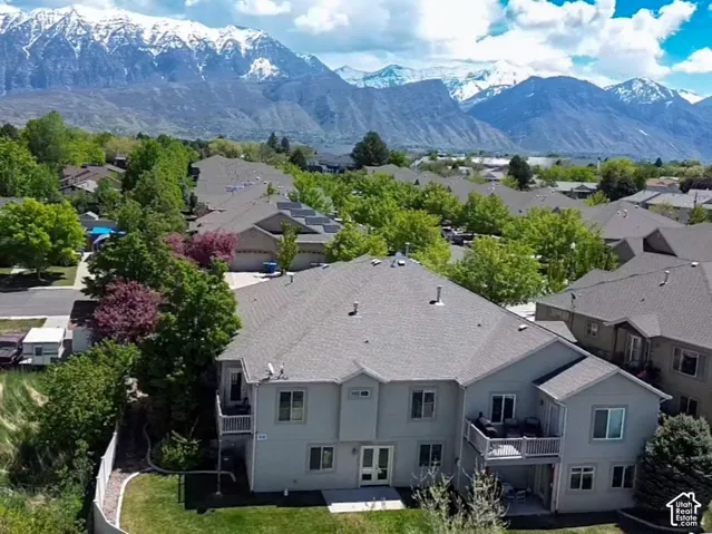 Aerial perspective featuring snow-capped mountain scenery, multi-level residential architecture, exterior upper-level balconies, and mature perimeter landscaping