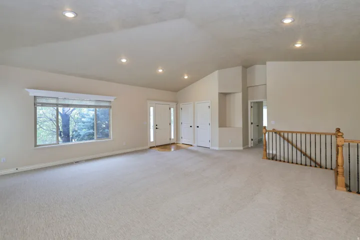 Vaulted ceiling with recessed lighting, light-toned carpeting, large window with transom, wood-finish flooring at entry, and wood and wrought iron staircase railing