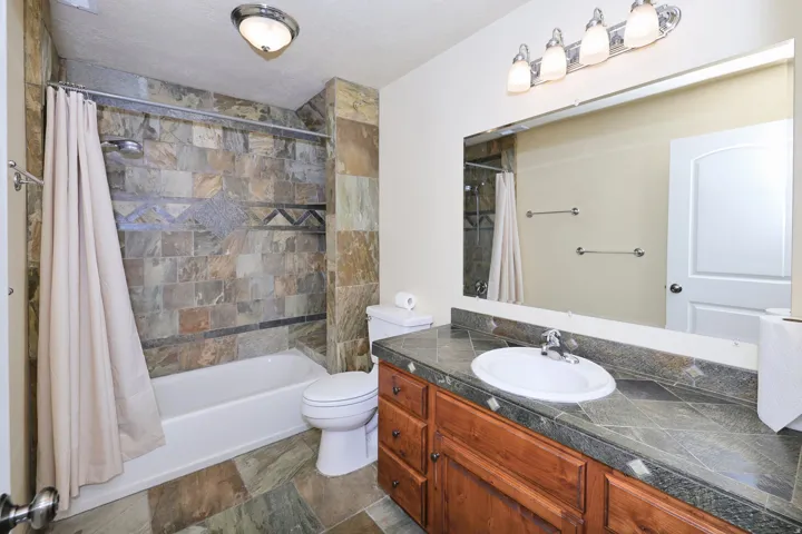 Bathroom featuring a built-in tub with tile surround, wood-finish vanity with an integrated sink, broad mirror, and overhead vanity lighting