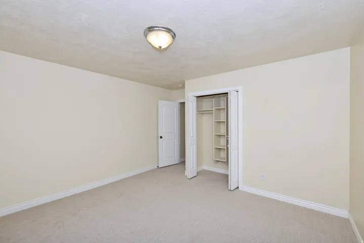 Neutral-toned carpet flooring, light-colored wall paint, white trim, and a built-in closet with shelving