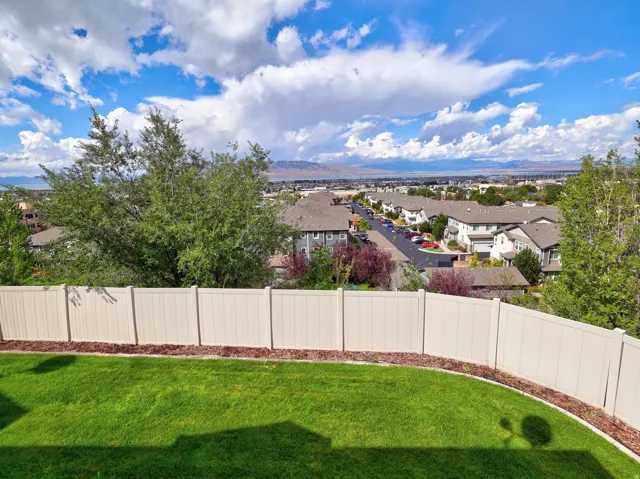 Expansive green lawn with a curved mulch border, enclosed by a perimeter fence, offering a high-elevation perspective of the surrounding residential area and distant mountains