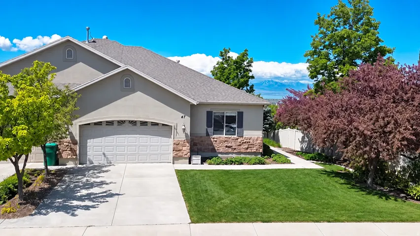 Stucco exterior with stone accent siding, attached two-car garage, concrete driveway, and manicured lawn