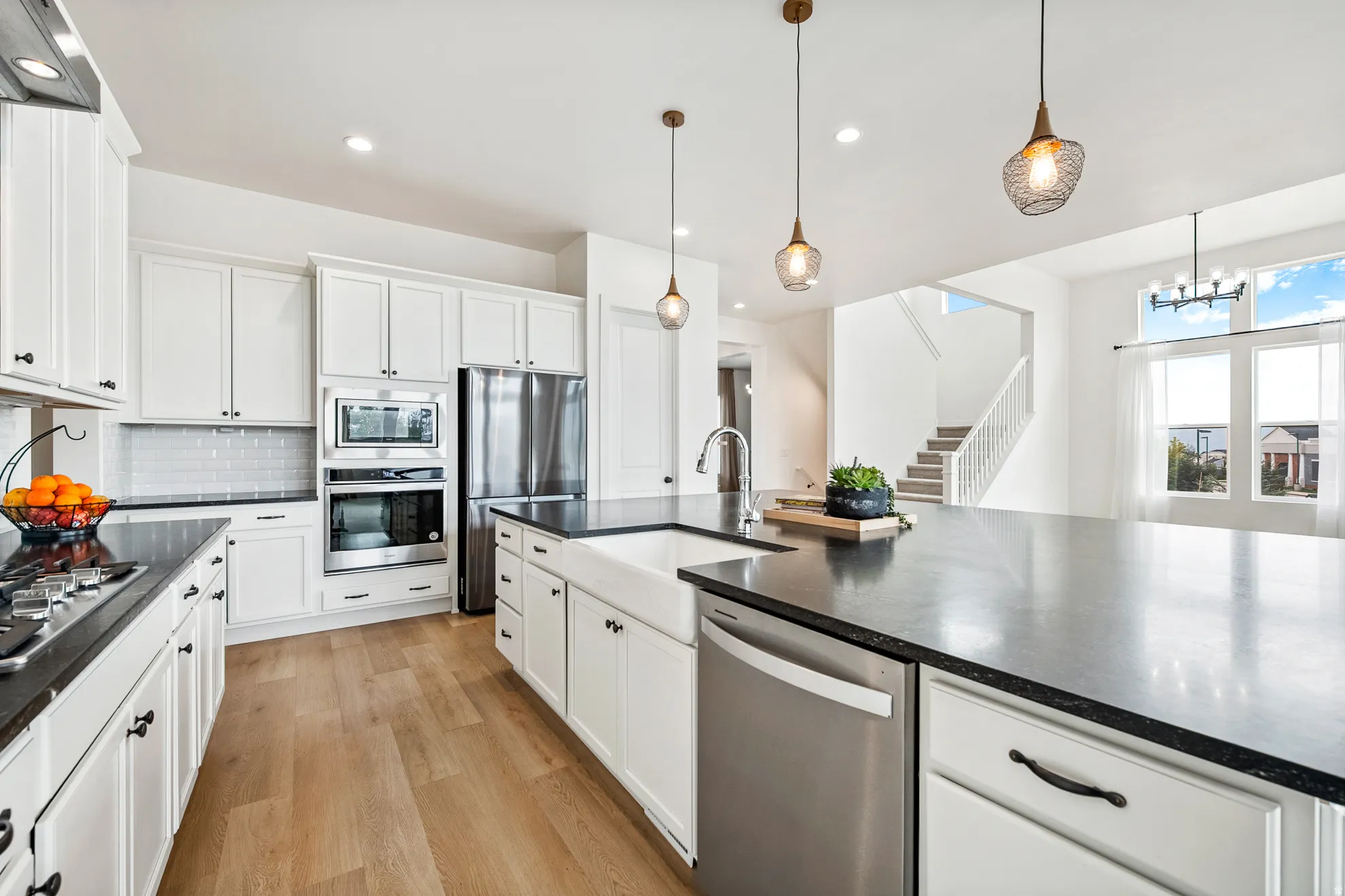Gourmet kitchen featuring white cabinetry, dark countertops, wood-finish flooring, stainless steel appliances, and a farmhouse sink