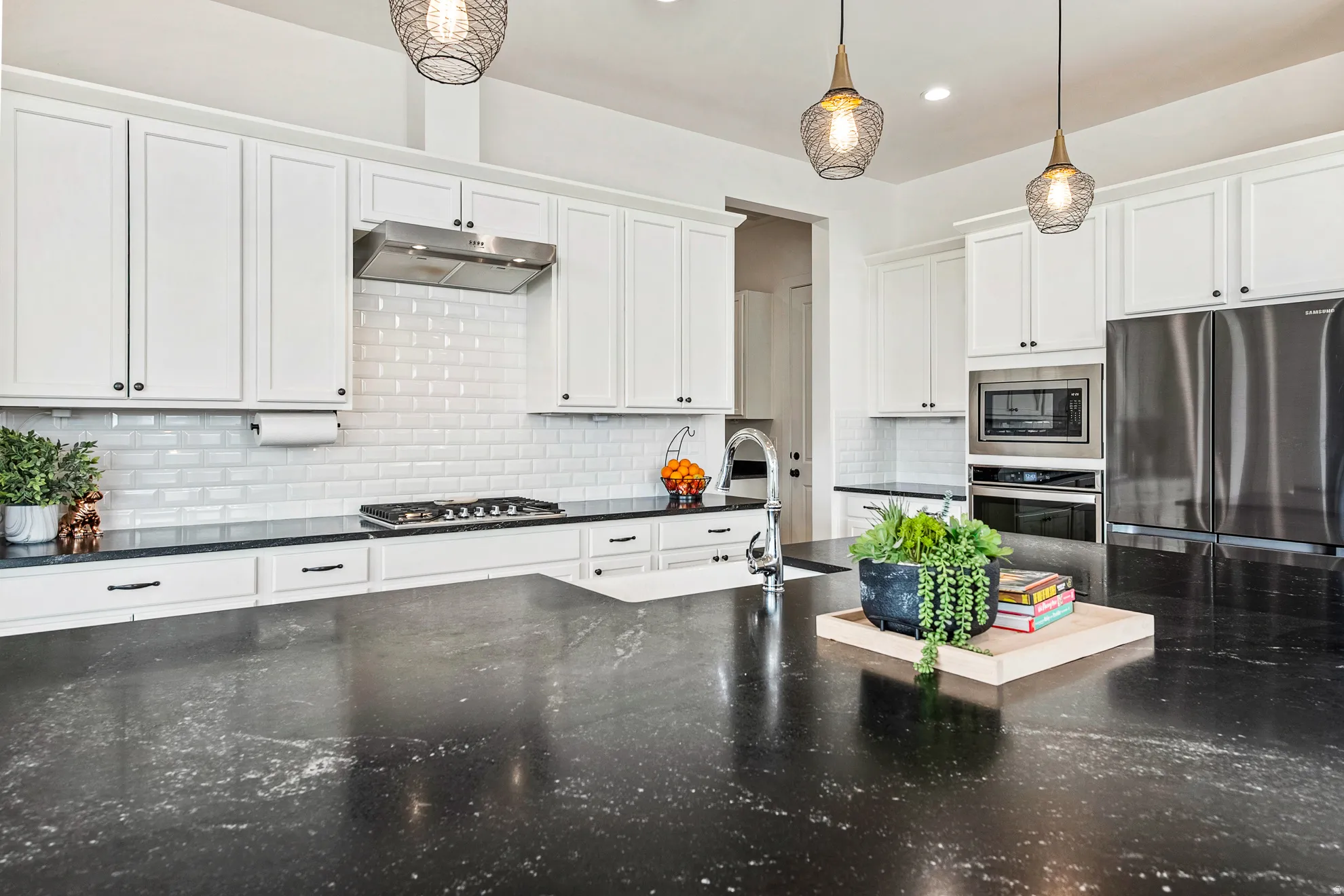 Expansive kitchen island with dark stone countertop, white shaker cabinetry, stainless steel appliances, and subway tile backsplash