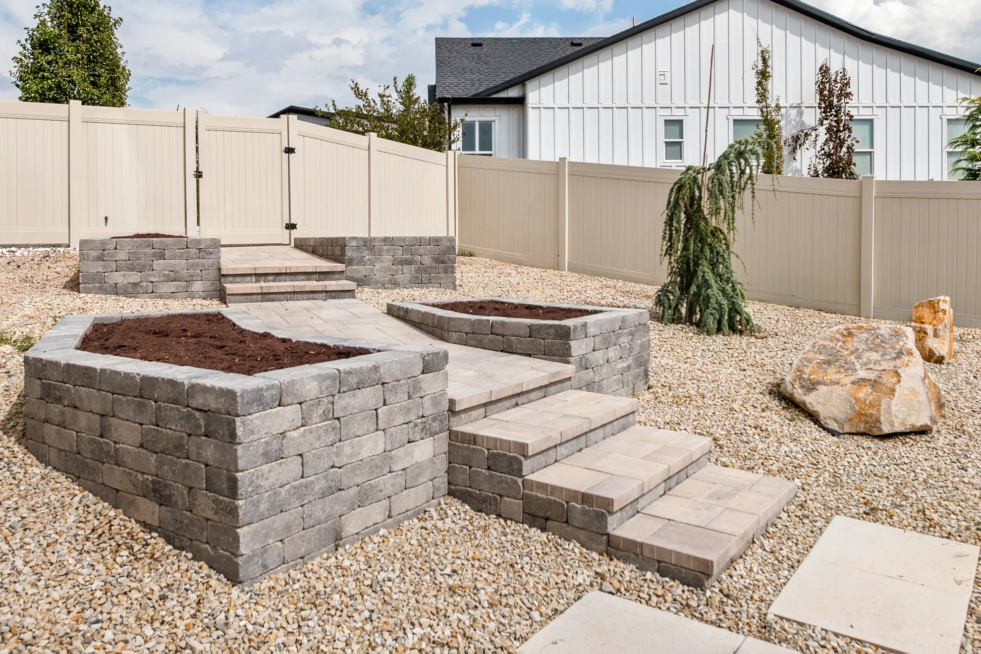 Landscaped backyard featuring stone-block raised garden beds and stone paver steps