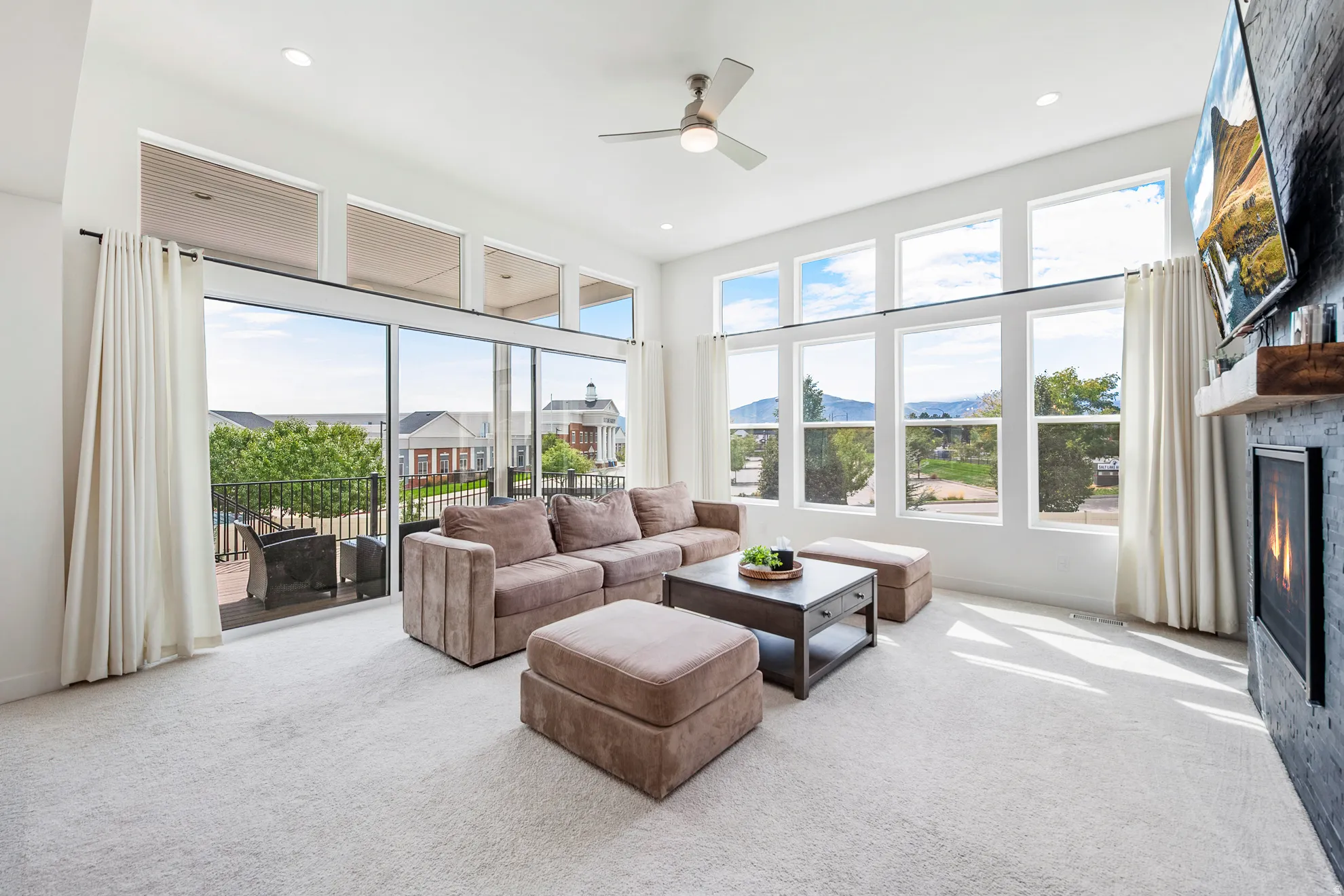 Spacious living area featuring expansive windows, high ceilings, a built-in fireplace with a dark-toned surround, and direct access to an outdoor balcony