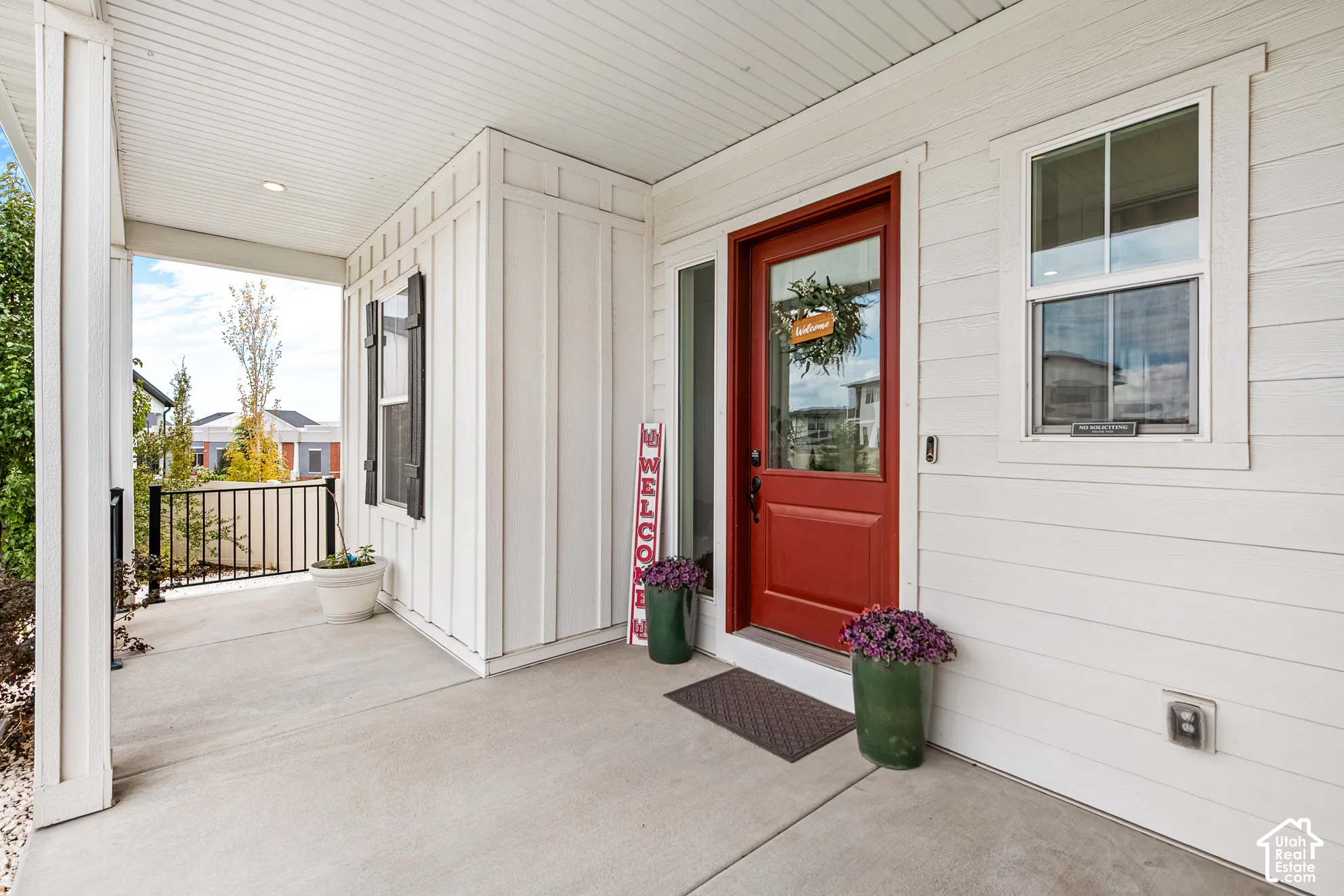 Covered concrete porch with white siding, red entry door with sidelight, and black accent shutters