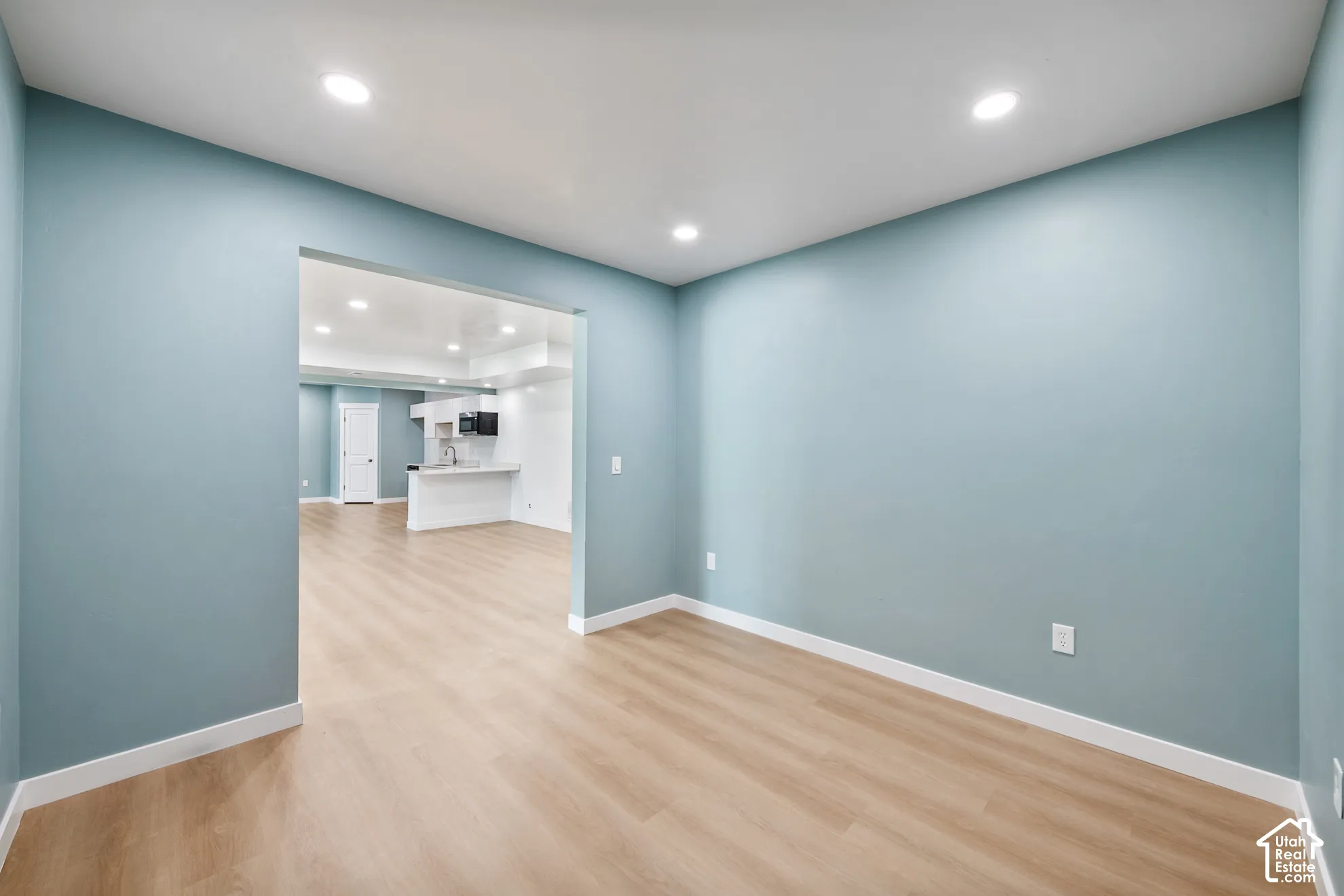 Recessed lighting, light wood-finish flooring, and a wide entryway to the kitchen featuring white cabinetry and appliances