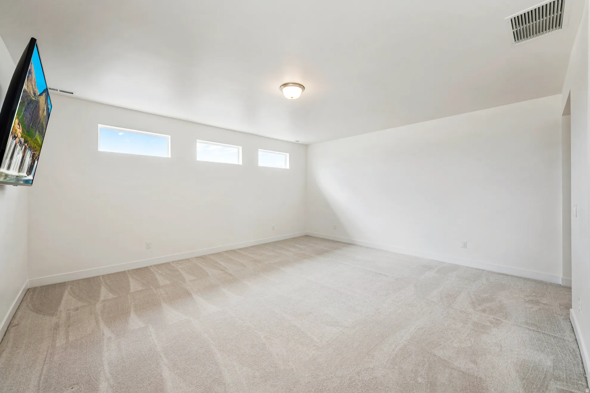 Recessed windows provide ample natural light within this expansive room, featuring neutral wall tones and a ceiling-mounted light fixture