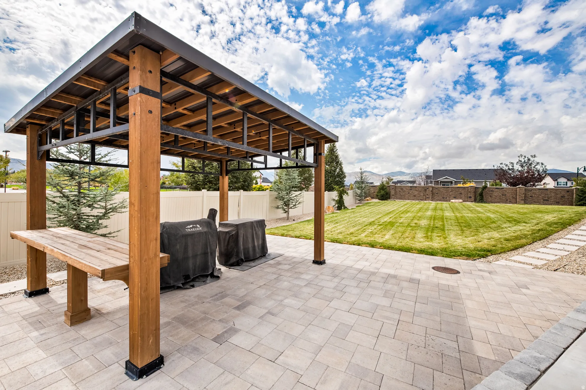 Patio featuring a wood pergola with metal roof, paver flooring, expansive lawn, and stone retaining wall